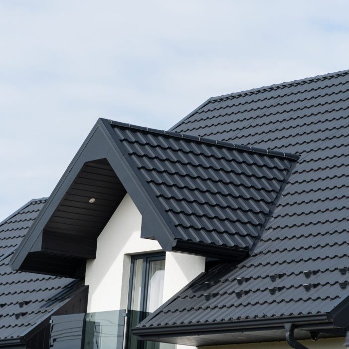 A beautiful modern house is covered with black metal tiles. Roofing of metal profile wavy shape.